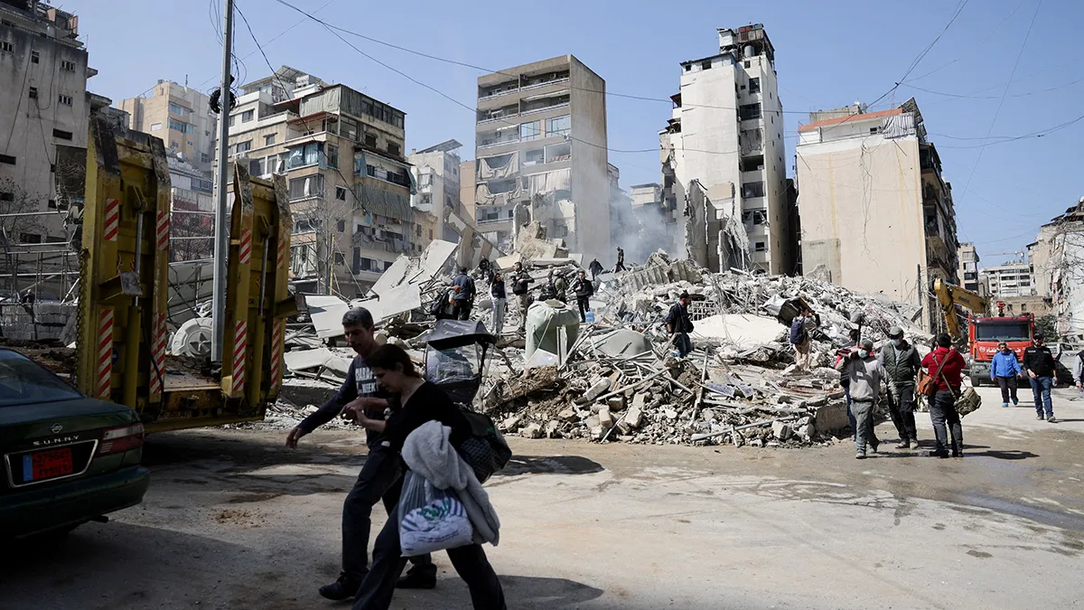 <p>Varias personas caminan junto a los escombros en el lugar donde se produjo un ataque israelí, tras la escalada de tensión entre Hezbolá e Israel en el marco del conflicto entre Estados Unidos e Israel con Irán, en el barrio de Zuqaq al-Blat, en el centro de Beirut (Líbano), el 18 de marzo de 2026 - REUTERS/ KHALIL ASHAWI</p>
