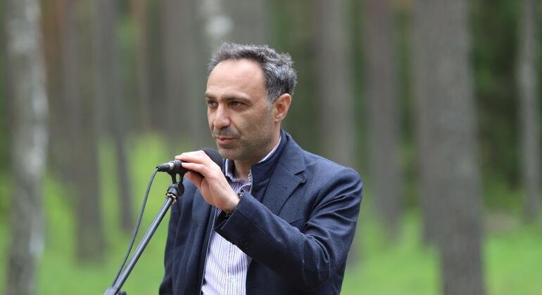 Un hombre de traje hablando en un micrófono en un bosque.
