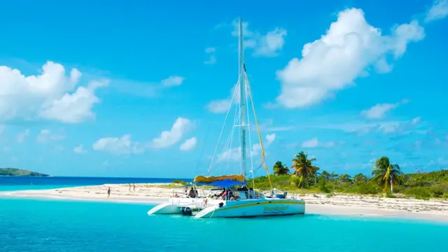 Embarcación en la orilla de la isla, de la que se ve algo de playa, palmeras pequeñas y vegetación, así como un puñado de personas caminando