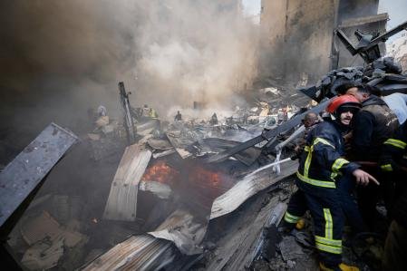 Bomberos, equipos de primera respuesta y voluntarios trabajan entre los restos humeantes en el lugar de un ataque aéreo israelí 