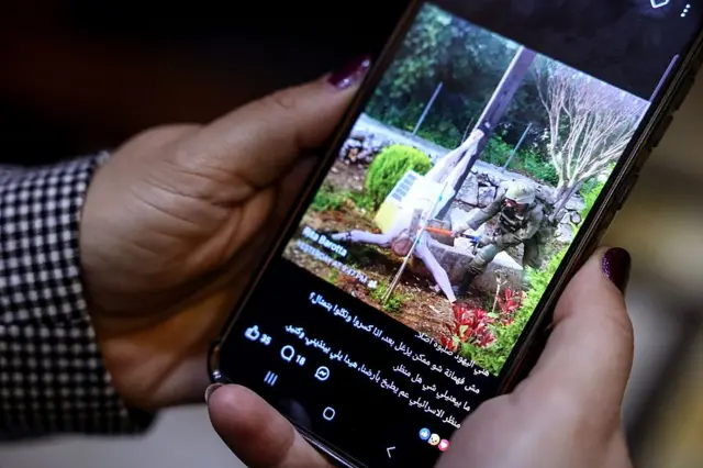 Las manos de una mujer sostienen un celular con la foto del soldado israelí golpeando la figura escultórica de Jesucristo y un texto en árabe