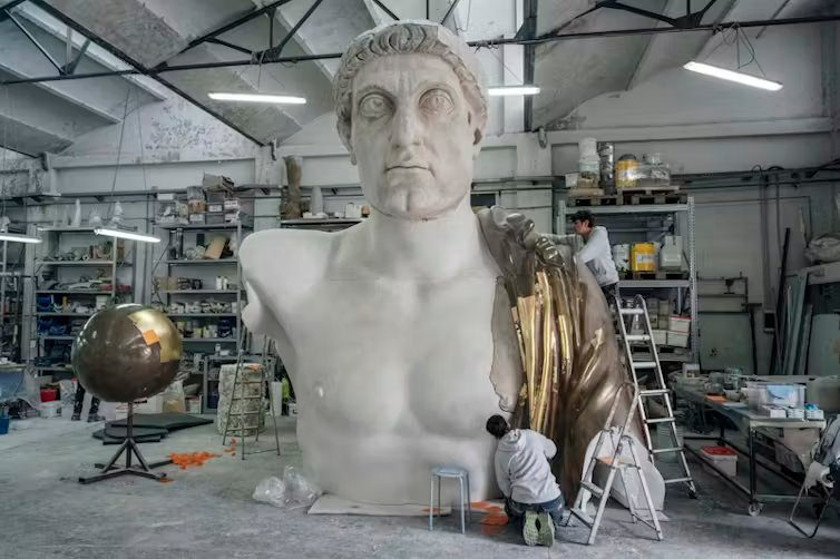 Varios obreros trabajan en la reconstrucción de una escultura colosal de un emperador romano.