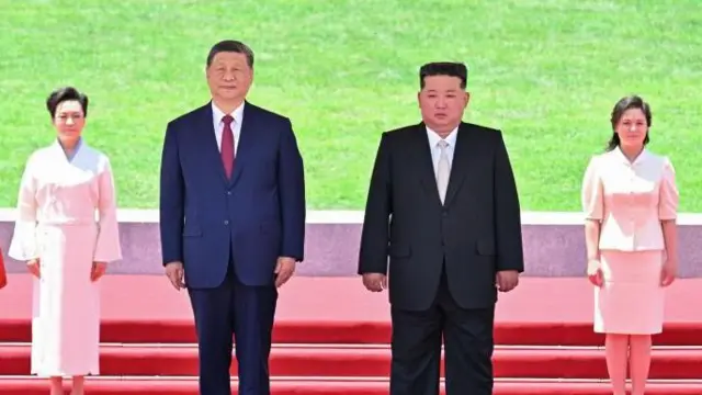 Xi (izquierda) y Kim (derecha) aparecen aquí de pie sobre un podio, con sus esposas detrás vestidas de blanco. 