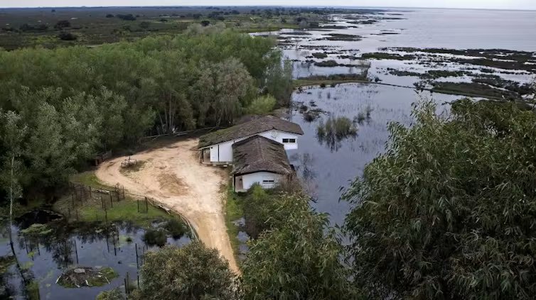 Dos casas con techo de paja en una franja de tierra con vegetación en medio de dos grandes lagunas
