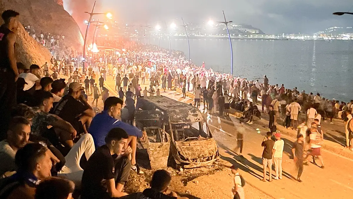 Un grupo de migrantes se reúne alrededor de un vehículo incendiado mientras esperan la oportunidad de cruzar al enclave español de Ceuta, en el lado marroquí de la frontera, en Fnideq (Marruecos), el 31 de julio de 2026. Fotografía tomada con un teléfono móvil - PHOTO/ REUTERS